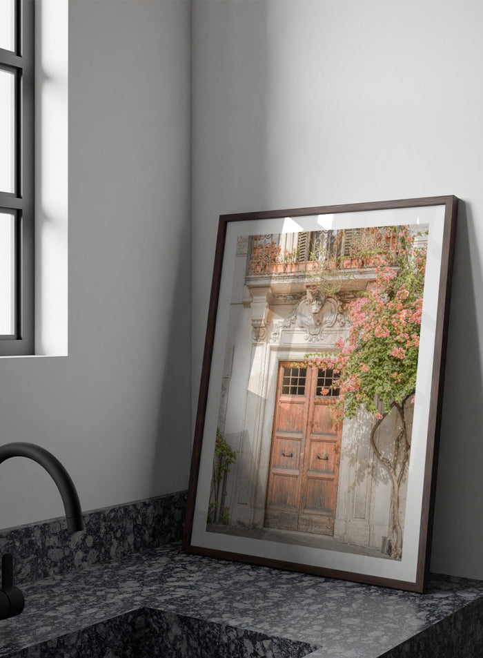 Wooden door with floral decorations on a building facade. Floral Entry by Henrike Schenk is a Mediterranean photography print featuring an old European doorway, blooming flowers, and historic architecture.
