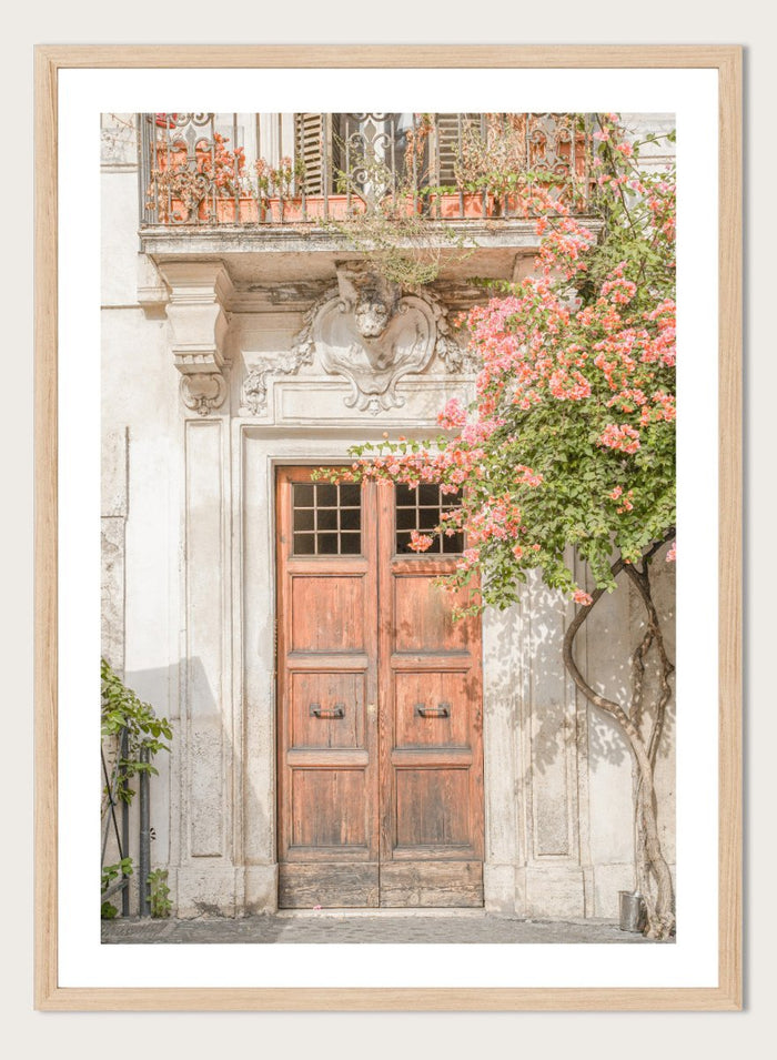 Wooden door with floral decorations on a building facade. Floral Entry by Henrike Schenk is a Mediterranean photography print featuring an old European doorway, blooming flowers, and historic architecture.
