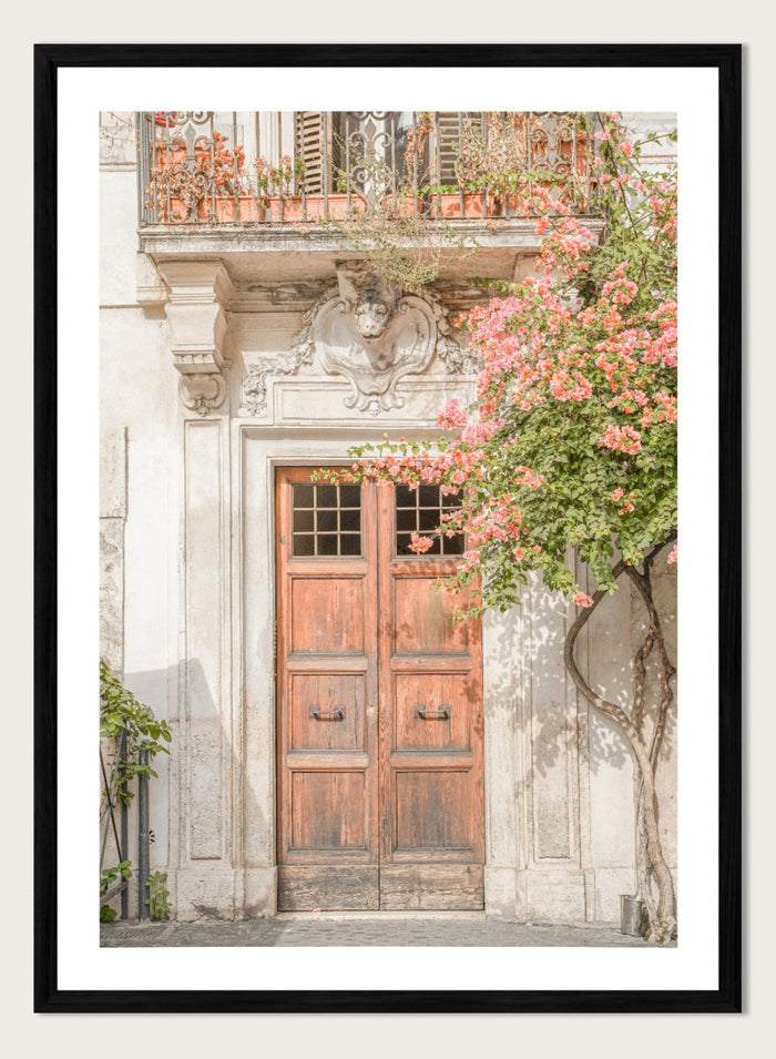 Wooden door with floral decorations on a building facade. Floral Entry by Henrike Schenk is a Mediterranean photography print featuring an old European doorway, blooming flowers, and historic architecture.