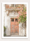 Wooden door with floral decorations on a building facade. Floral Entry by Henrike Schenk is a Mediterranean photography print featuring an old European doorway, blooming flowers, and historic architecture.