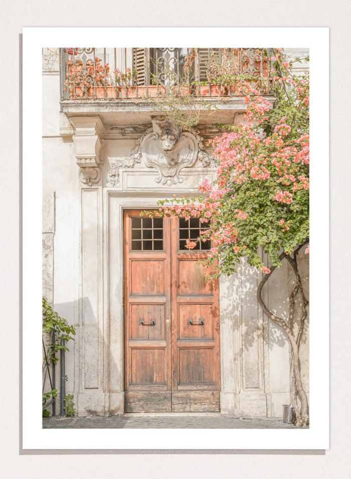 Wooden door with floral decorations on a building facade. Floral Entry by Henrike Schenk is a Mediterranean photography print featuring an old European doorway, blooming flowers, and historic architecture.