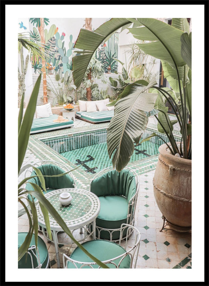 Outdoor patio with pool, green chairs, and potted plants. Green Courtyard Oasis by Henrike Schenk is a Morocco travel photography print showing a lush riad courtyard with green tilework, tropical plants, and poolside interiors.