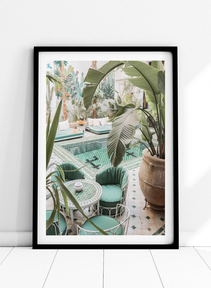 Outdoor patio with pool, green chairs, and potted plants. Green Courtyard Oasis by Henrike Schenk is a Morocco travel photography print showing a lush riad courtyard with green tilework, tropical plants, and poolside interiors.