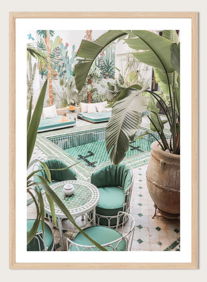 Outdoor patio with pool, green chairs, and potted plants. Green Courtyard Oasis by Henrike Schenk is a Morocco travel photography print showing a lush riad courtyard with green tilework, tropical plants, and poolside interiors.