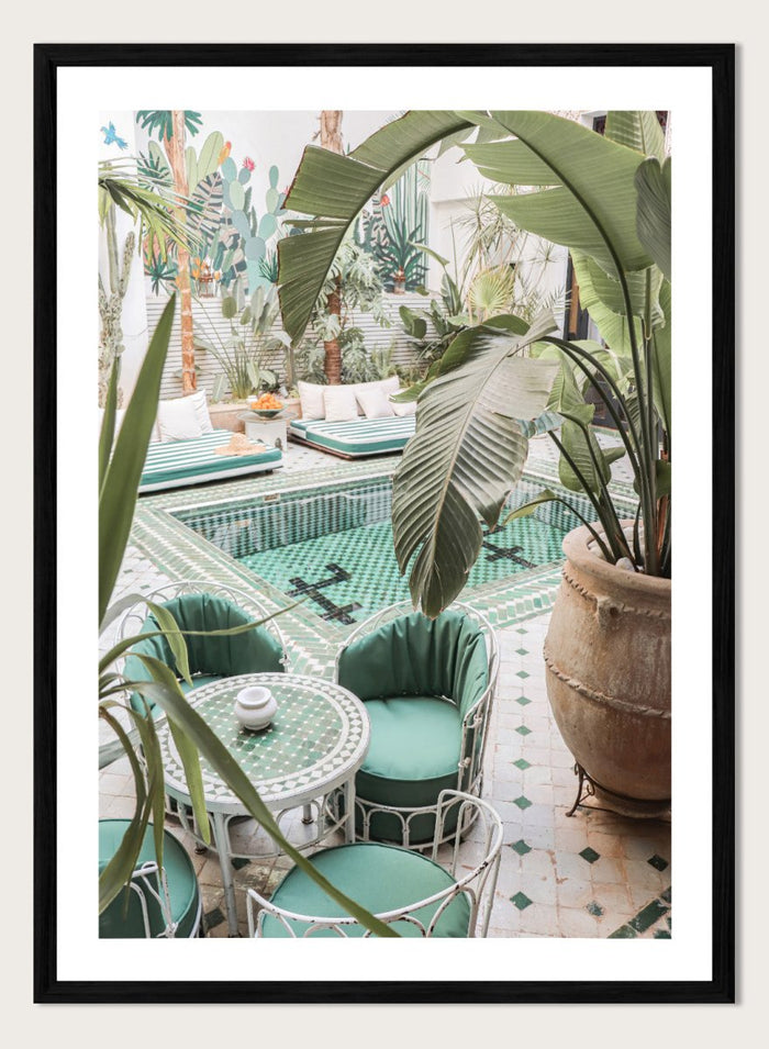 Outdoor patio with pool, green chairs, and potted plants. Green Courtyard Oasis by Henrike Schenk is a Morocco travel photography print showing a lush riad courtyard with green tilework, tropical plants, and poolside interiors.