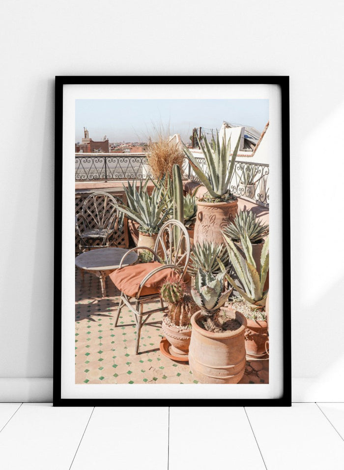 Potted plants on a balcony with a cityscape in the background. Moroccan Cactus Patio by Henrike Schenk captures a Moroccan rooftop terrace with cacti, terracotta pots, and desert-inspired photography wall art.