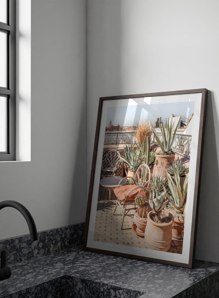 Potted plants on a balcony with a cityscape in the background. Moroccan Cactus Patio by Henrike Schenk captures a Moroccan rooftop terrace with cacti, terracotta pots, and desert-inspired photography wall art.