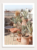Potted plants on a balcony with a cityscape in the background. Moroccan Cactus Patio by Henrike Schenk captures a Moroccan rooftop terrace with cacti, terracotta pots, and desert-inspired photography wall art.