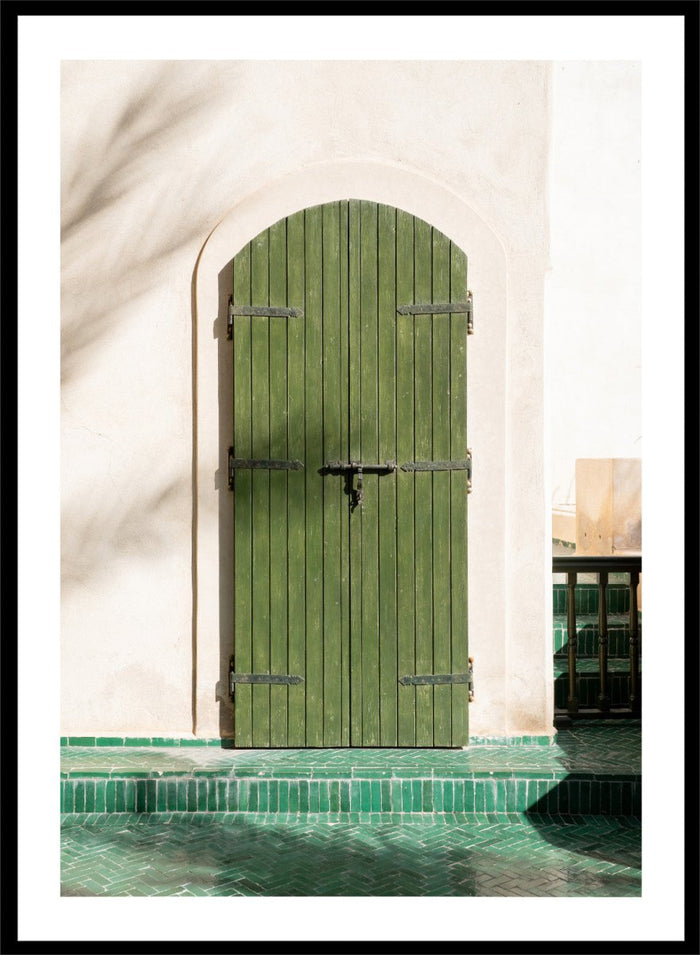 Green wooden door with metal latch on a white wall next to a pool. Moroccan Green Door by Henrike Schenk is an architectural photography print featuring green tilework, a traditional doorway, and Moroccan design details.