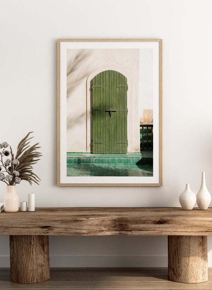 Green wooden door with metal latch on a white wall next to a pool. Moroccan Green Door by Henrike Schenk is an architectural photography print featuring green tilework, a traditional doorway, and Moroccan design details.