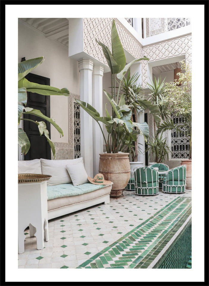 Outdoor patio with white sofa, green chairs, and potted plants in a decorative courtyard. Moroccan Riad Courtyard Oasis by Henrike Schenk is a Morocco photography print of a riad courtyard with tropical plants, tilework, and interior decor.