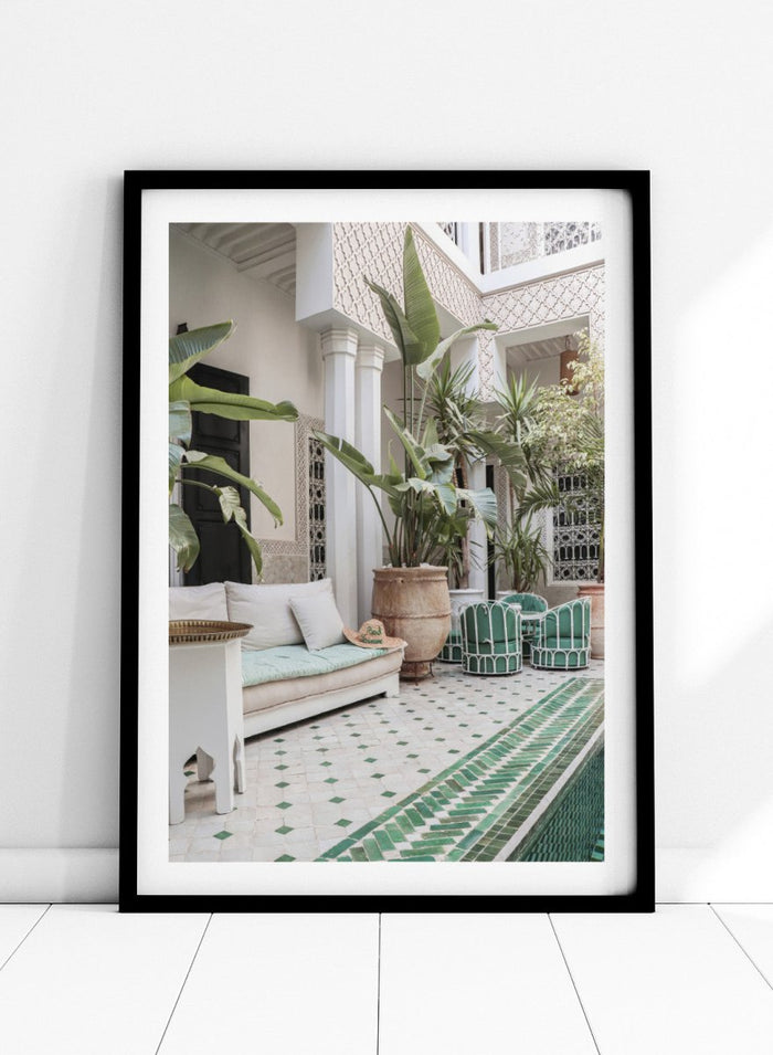 Outdoor patio with white sofa, green chairs, and potted plants in a decorative courtyard. Moroccan Riad Courtyard Oasis by Henrike Schenk is a Morocco photography print of a riad courtyard with tropical plants, tilework, and interior decor.