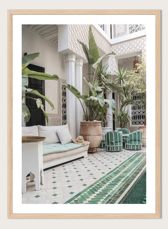 Outdoor patio with white sofa, green chairs, and potted plants in a decorative courtyard. Moroccan Riad Courtyard Oasis by Henrike Schenk is a Morocco photography print of a riad courtyard with tropical plants, tilework, and interior decor.