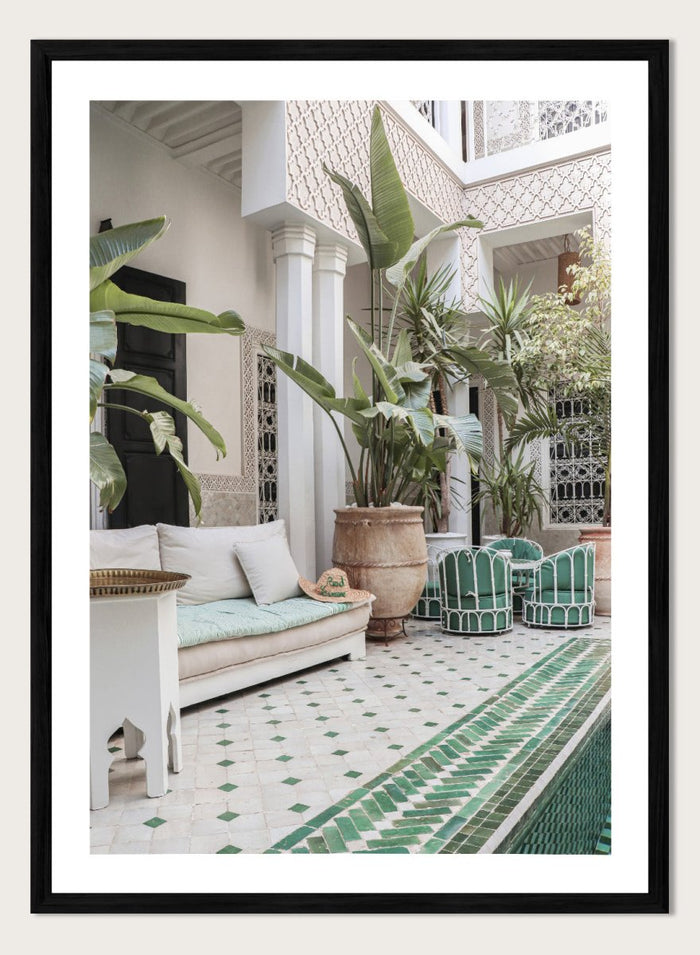 Outdoor patio with white sofa, green chairs, and potted plants in a decorative courtyard. Moroccan Riad Courtyard Oasis by Henrike Schenk is a Morocco photography print of a riad courtyard with tropical plants, tilework, and interior decor.