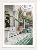 Outdoor patio with white sofa, green chairs, and potted plants in a decorative courtyard. Moroccan Riad Courtyard Oasis by Henrike Schenk is a Morocco photography print of a riad courtyard with tropical plants, tilework, and interior decor.