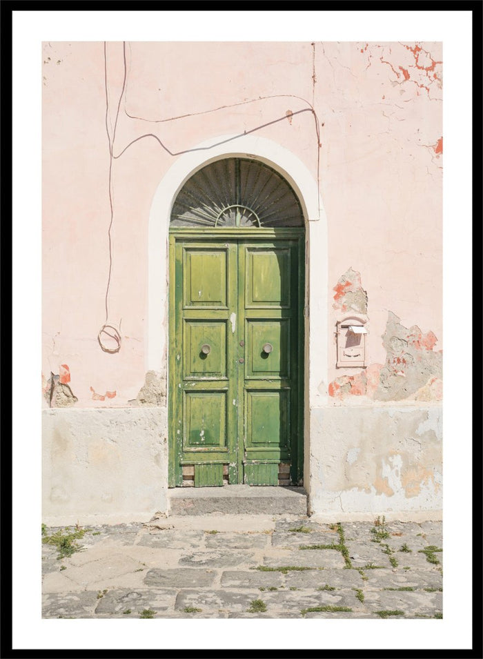 Green door on a pink wall with peeling paint. Old World Green Door by Henrike Schenk features a vintage European doorway, weathered architecture, pastel walls, travel photography, and wall art.