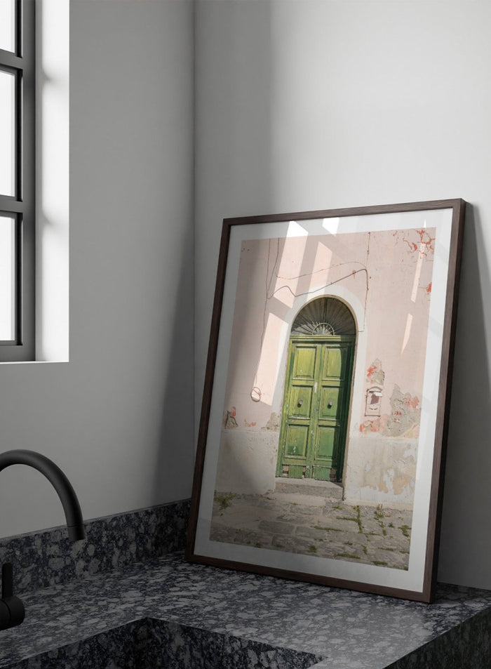 Green door on a pink wall with peeling paint. Old World Green Door by Henrike Schenk features a vintage European doorway, weathered architecture, pastel walls, travel photography, and wall art.