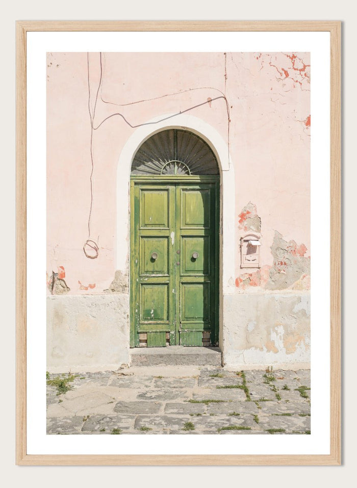 Green door on a pink wall with peeling paint. Old World Green Door by Henrike Schenk features a vintage European doorway, weathered architecture, pastel walls, travel photography, and wall art.