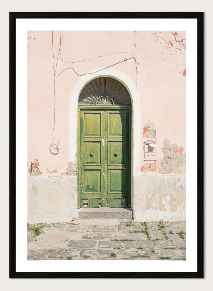 Green door on a pink wall with peeling paint. Old World Green Door by Henrike Schenk features a vintage European doorway, weathered architecture, pastel walls, travel photography, and wall art.