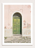 Green door on a pink wall with peeling paint. Old World Green Door by Henrike Schenk features a vintage European doorway, weathered architecture, pastel walls, travel photography, and wall art.