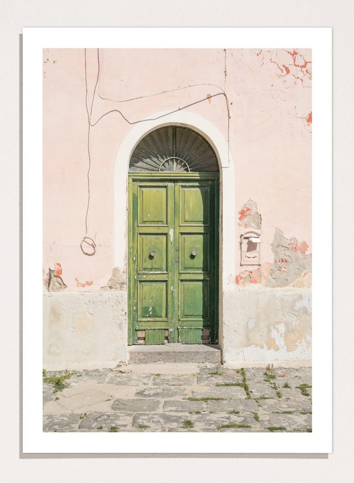 Green door on a pink wall with peeling paint. Old World Green Door by Henrike Schenk features a vintage European doorway, weathered architecture, pastel walls, travel photography, and wall art.