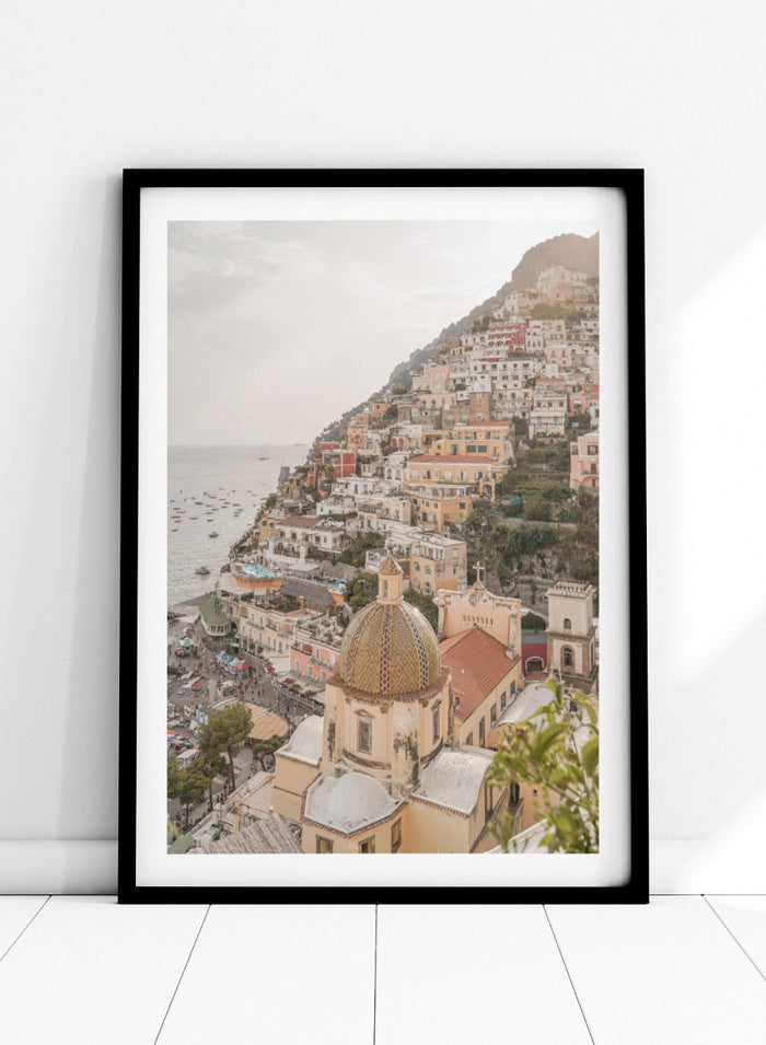 Hilly coastal town with buildings and a church dome. Positano Bliss by Henrike Schenk is a coastal photography print featuring the colorful hillside of Positano, Mediterranean architecture, and the beauty of the Amalfi Coast.