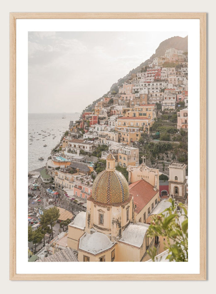 Hilly coastal town with buildings and a church dome. Positano Bliss by Henrike Schenk is a coastal photography print featuring the colorful hillside of Positano, Mediterranean architecture, and the beauty of the Amalfi Coast.