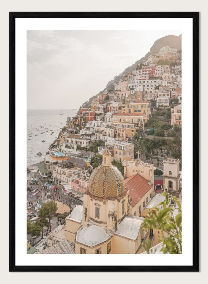 Hilly coastal town with buildings and a church dome. Positano Bliss by Henrike Schenk is a coastal photography print featuring the colorful hillside of Positano, Mediterranean architecture, and the beauty of the Amalfi Coast.