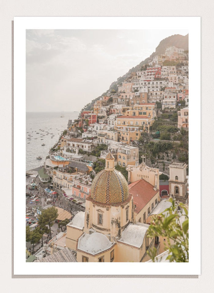 Hilly coastal town with buildings and a church dome. Positano Bliss by Henrike Schenk is a coastal photography print featuring the colorful hillside of Positano, Mediterranean architecture, and the beauty of the Amalfi Coast.