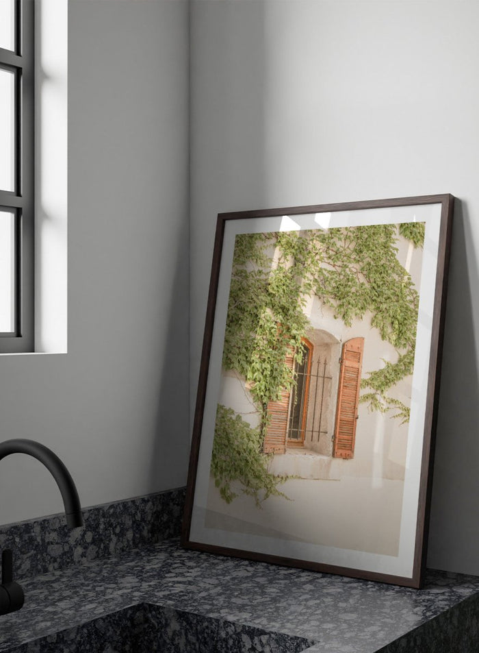 Window with wooden shutters framed by climbing ivy on a light-colored wall. Rustic Window With Ivy by Henrike Schenk is a European photography print featuring historic architecture, blooming flowers, and Mediterranean charm.