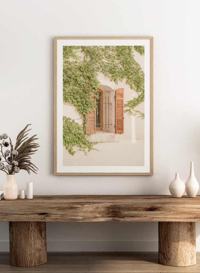 Window with wooden shutters framed by climbing ivy on a light-colored wall. Rustic Window With Ivy by Henrike Schenk is a European photography print featuring historic architecture, blooming flowers, and Mediterranean charm.