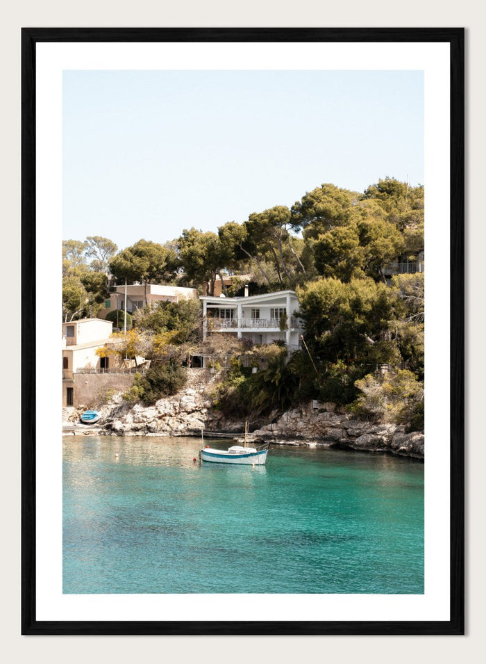 Cottage by a lake with trees and boats in the water. Serene Mediterranean Cove by Henrike Schenk is a coastal photography print featuring turquoise water, a fishing boat, seaside homes, and Mediterranean scenery.