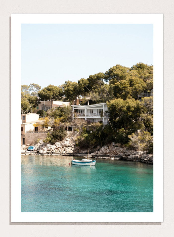 Cottage by a lake with trees and boats in the water. Serene Mediterranean Cove by Henrike Schenk is a coastal photography print featuring turquoise water, a fishing boat, seaside homes, and Mediterranean scenery.