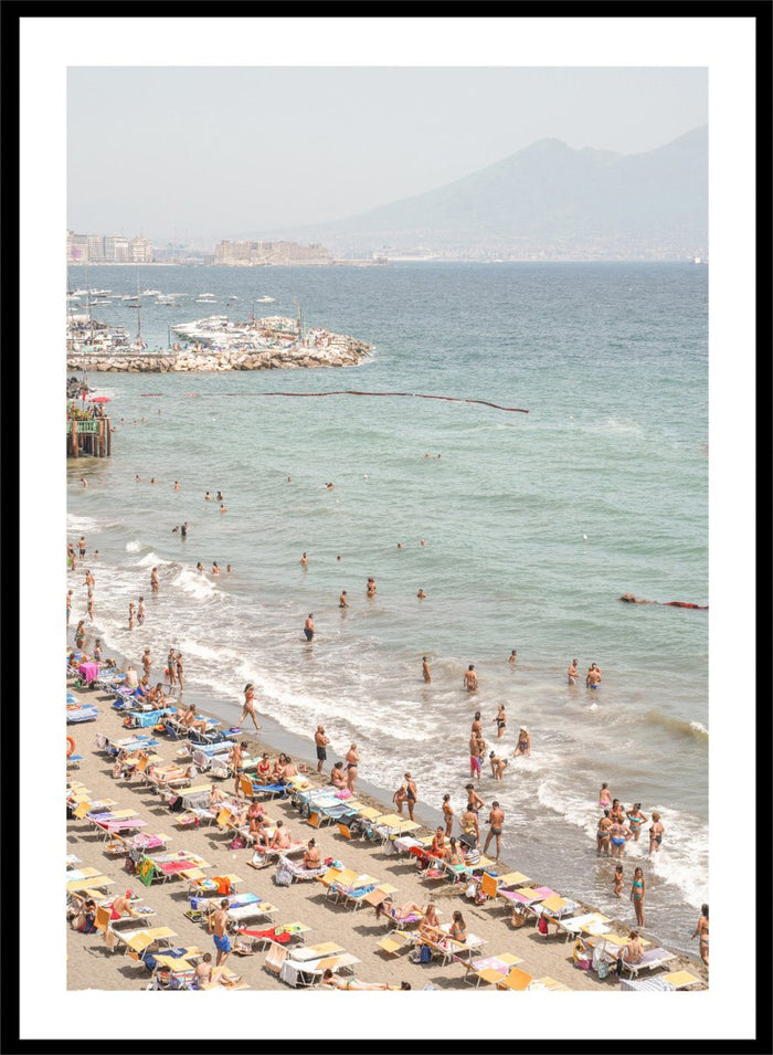 Beach scene with people and umbrellas near a body of water with mountains in the background. Summer Beach Mountain View by Henrike Schenk is a Mediterranean beach photography print featuring coastal views, mountains, ocean scenery, and summer travel.