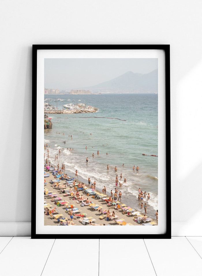 Beach scene with people and umbrellas near a body of water with mountains in the background. Summer Beach Mountain View by Henrike Schenk is a Mediterranean beach photography print featuring coastal views, mountains, ocean scenery, and summer travel.
