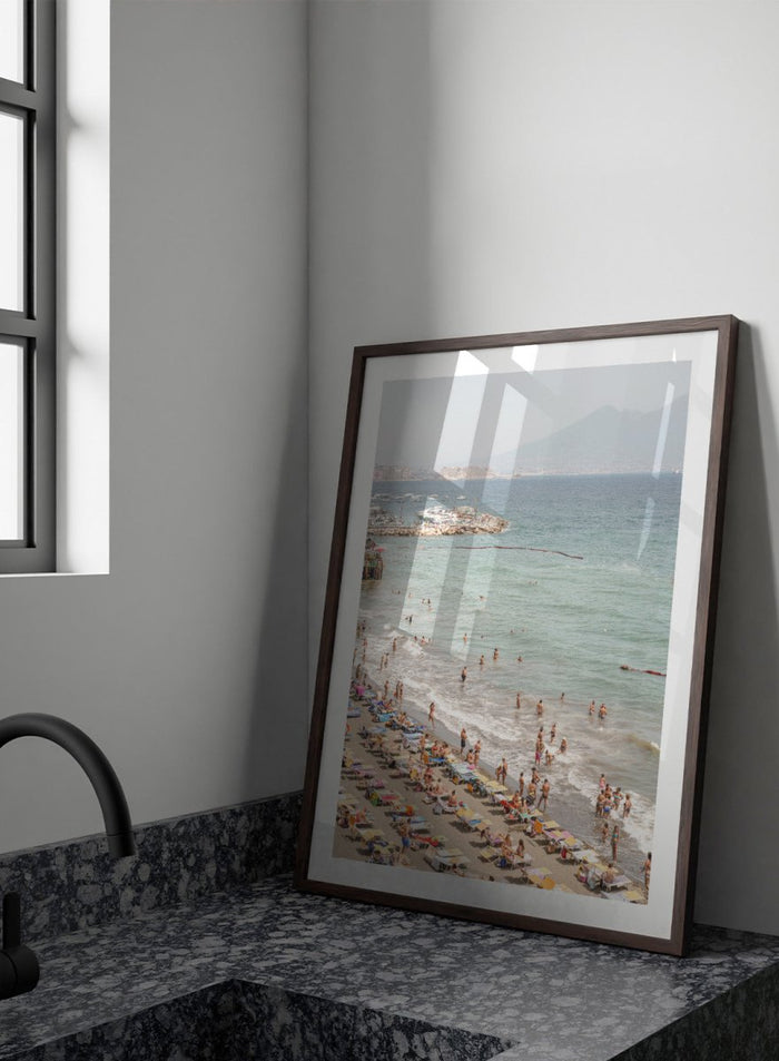 Beach scene with people and umbrellas near a body of water with mountains in the background. Summer Beach Mountain View by Henrike Schenk is a Mediterranean beach photography print featuring coastal views, mountains, ocean scenery, and summer travel.