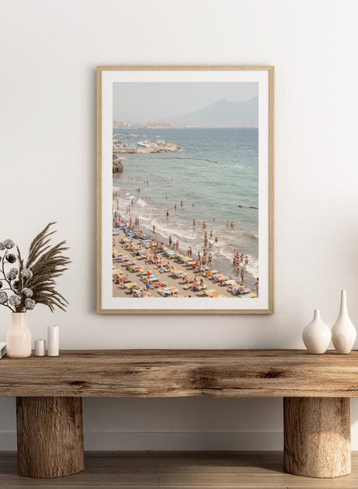 Beach scene with people and umbrellas near a body of water with mountains in the background. Summer Beach Mountain View by Henrike Schenk is a Mediterranean beach photography print featuring coastal views, mountains, ocean scenery, and summer travel.
