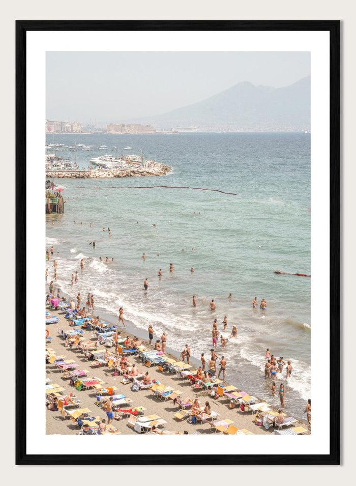 Beach scene with people and umbrellas near a body of water with mountains in the background. Summer Beach Mountain View by Henrike Schenk is a Mediterranean beach photography print featuring coastal views, mountains, ocean scenery, and summer travel.