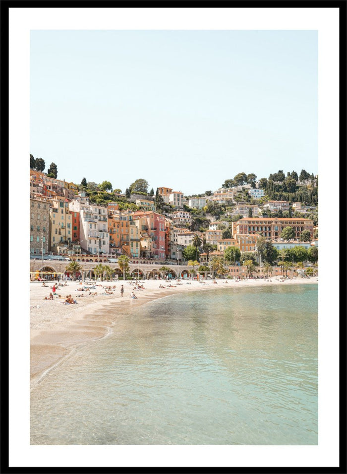 Coastal town with colorful buildings and a beach. Sunny Mediterranean Coast by Henrike Schenk is a coastal photography print featuring turquoise water, pastel buildings, Mediterranean beach scenery, and travel wall art.