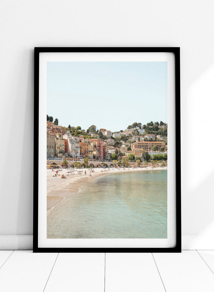 Coastal town with colorful buildings and a beach. Sunny Mediterranean Coast by Henrike Schenk is a coastal photography print featuring turquoise water, pastel buildings, Mediterranean beach scenery, and travel wall art.