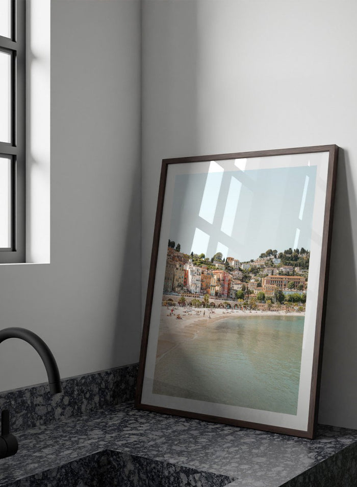 Coastal town with colorful buildings and a beach. Sunny Mediterranean Coast by Henrike Schenk is a coastal photography print featuring turquoise water, pastel buildings, Mediterranean beach scenery, and travel wall art.