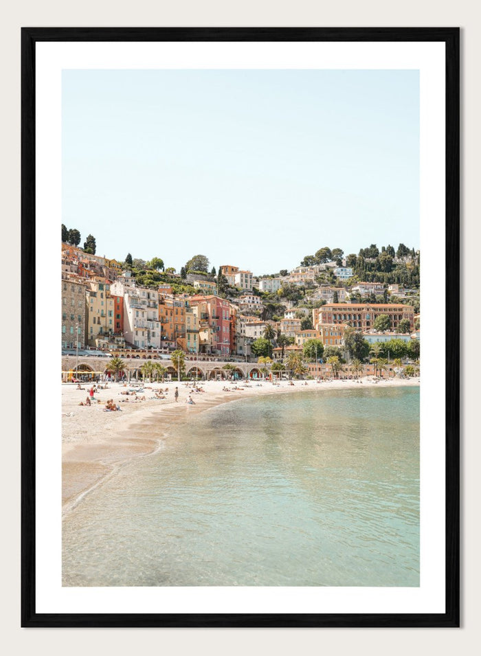 Coastal town with colorful buildings and a beach. Sunny Mediterranean Coast by Henrike Schenk is a coastal photography print featuring turquoise water, pastel buildings, Mediterranean beach scenery, and travel wall art.