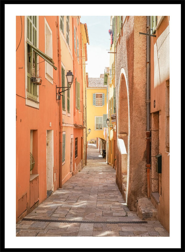 narrow street with colorful buildings in a European city. Vibrant European Alley by Henrike Schenk is a travel photography print featuring a Mediterranean street, cobblestone alley, and pastel European architecture.