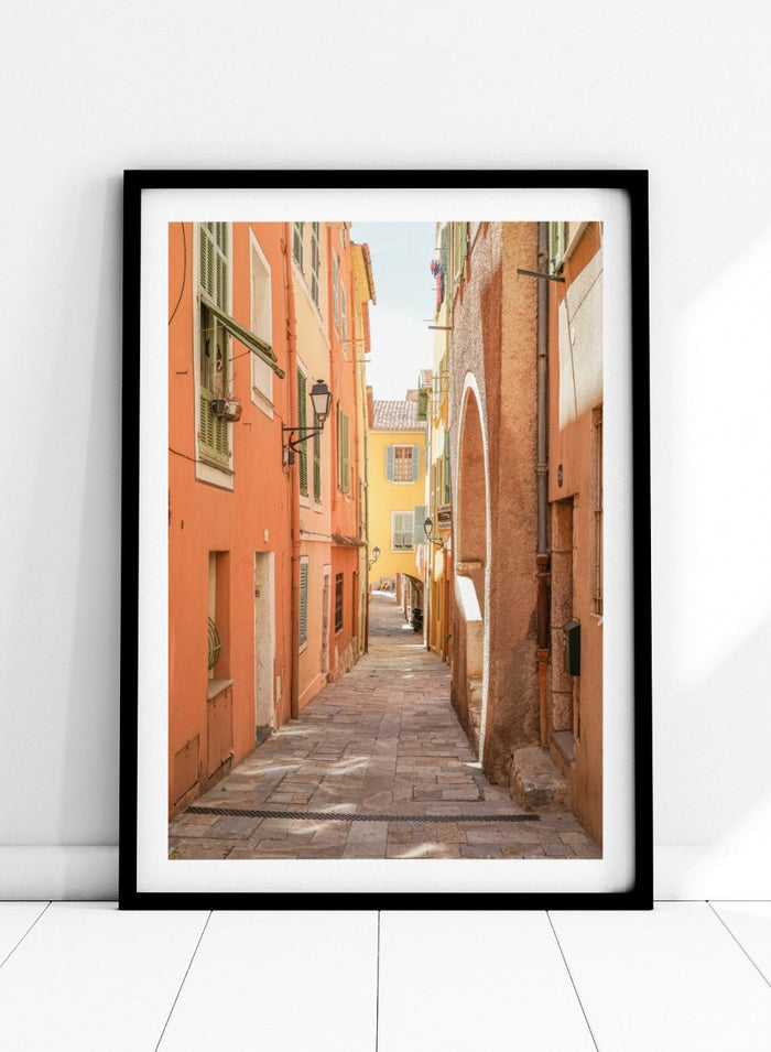narrow street with colorful buildings in a European city. Vibrant European Alley by Henrike Schenk is a travel photography print featuring a Mediterranean street, cobblestone alley, and pastel European architecture.