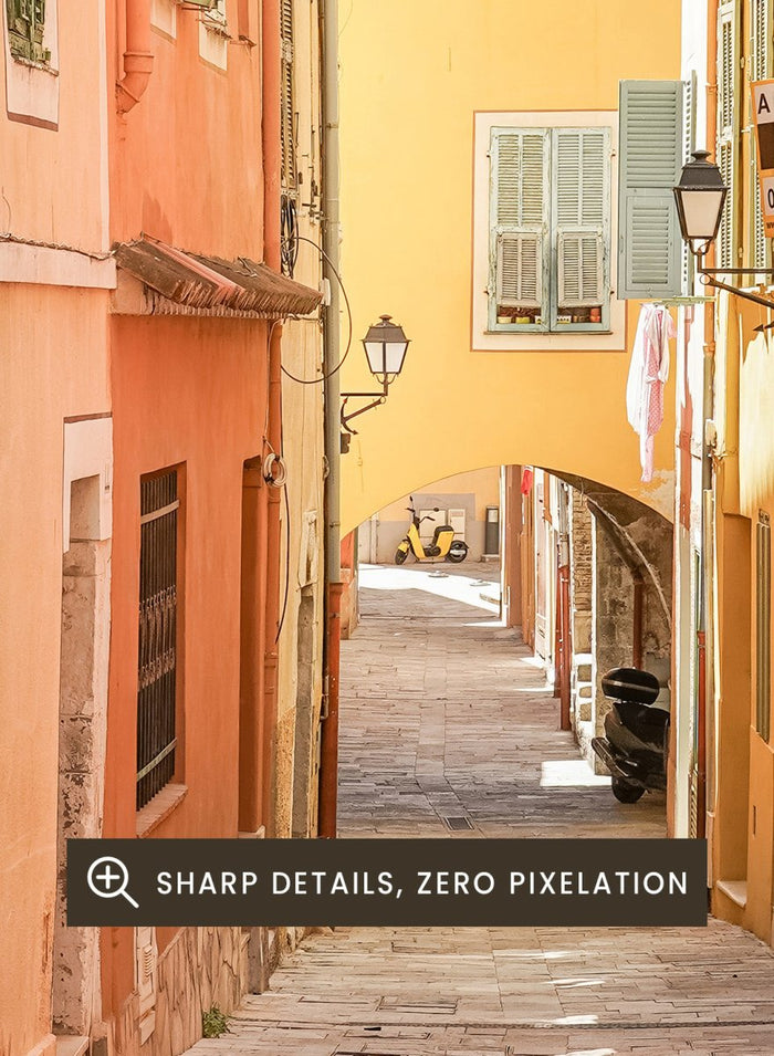 Framed photograph of a narrow street on a wall next to a window.  narrow street with colorful buildings in a European city. Vibrant European Alley by Henrike Schenk is a travel photography print featuring a Mediterranean street, cobblestone alley, and pastel European architecture.