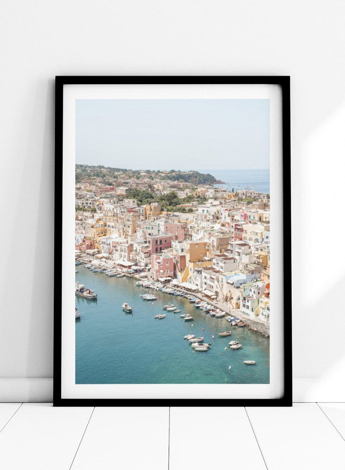 Coastal town with colorful buildings and boats in a harbor. Vibrant Italian Coastal Town by Henrike Schenk is a coastal photography print featuring pastel architecture, turquoise waters, fishing boats, and Mediterranean charm.