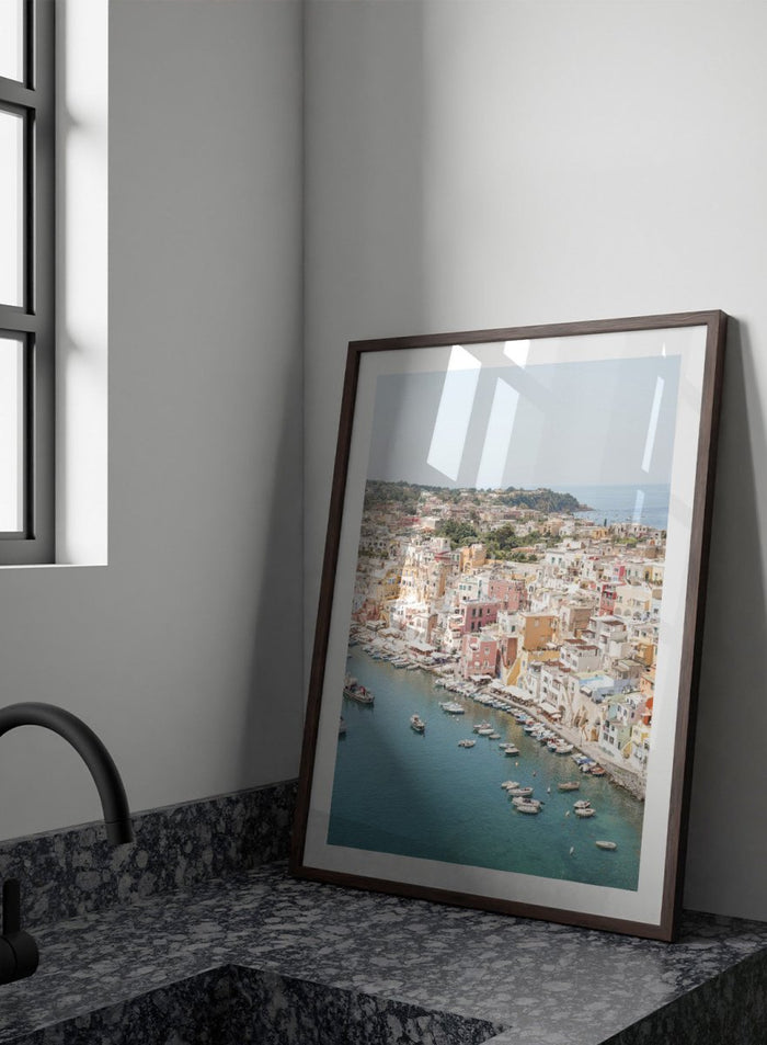 Coastal town with colorful buildings and boats in a harbor. Vibrant Italian Coastal Town by Henrike Schenk is a coastal photography print featuring pastel architecture, turquoise waters, fishing boats, and Mediterranean charm.