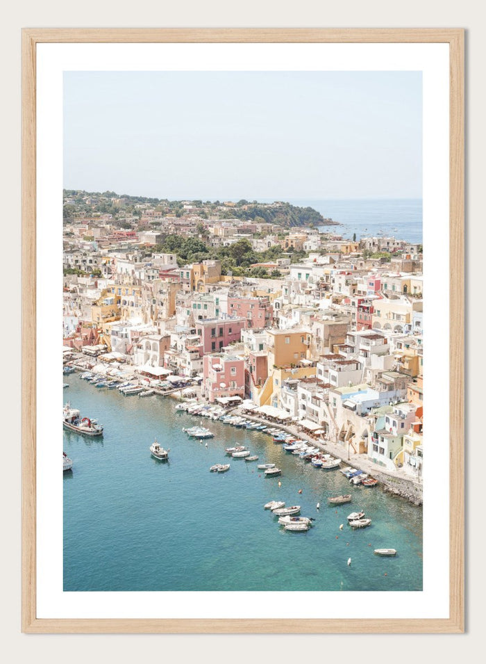Coastal town with colorful buildings and boats in a harbor. Vibrant Italian Coastal Town by Henrike Schenk is a coastal photography print featuring pastel architecture, turquoise waters, fishing boats, and Mediterranean charm.
