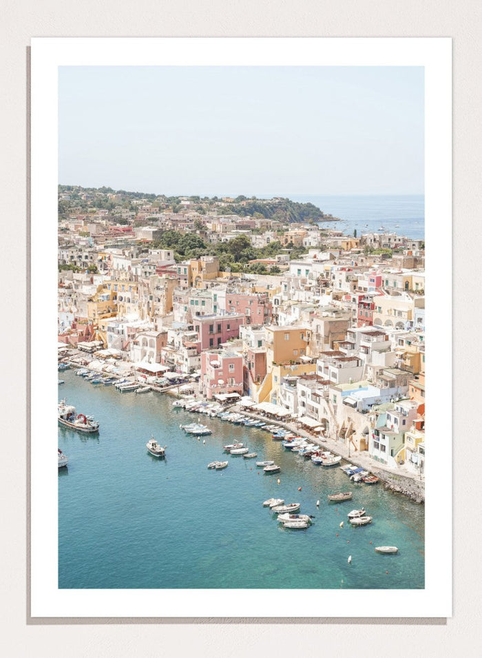 Coastal town with colorful buildings and boats in a harbor. Vibrant Italian Coastal Town by Henrike Schenk is a coastal photography print featuring pastel architecture, turquoise waters, fishing boats, and Mediterranean charm.