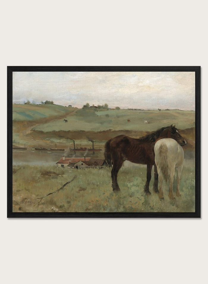 A framed landscape painting depicting two horses in a grassy field, with a muted sky and distant hills. Horses in a Meadow by Edgar Degas is a vintage horse art print featuring two horses standing together in a green field with a river, hills, and distant village.
